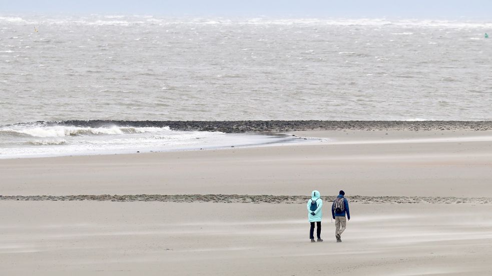 Bei stürmischem Wetter laufen Spaziergänger am Strand der Insel Norderney. Der Deutsche Wetterdienst erwartete am Donnerstag auf den Ostfriesischen Inseln schwere Sturmböen. Wegen Niedrigwassers bei dem starken Ostwind fielen mehrere Fährverbindungen aus. Foto: Volker Bartels/dpa