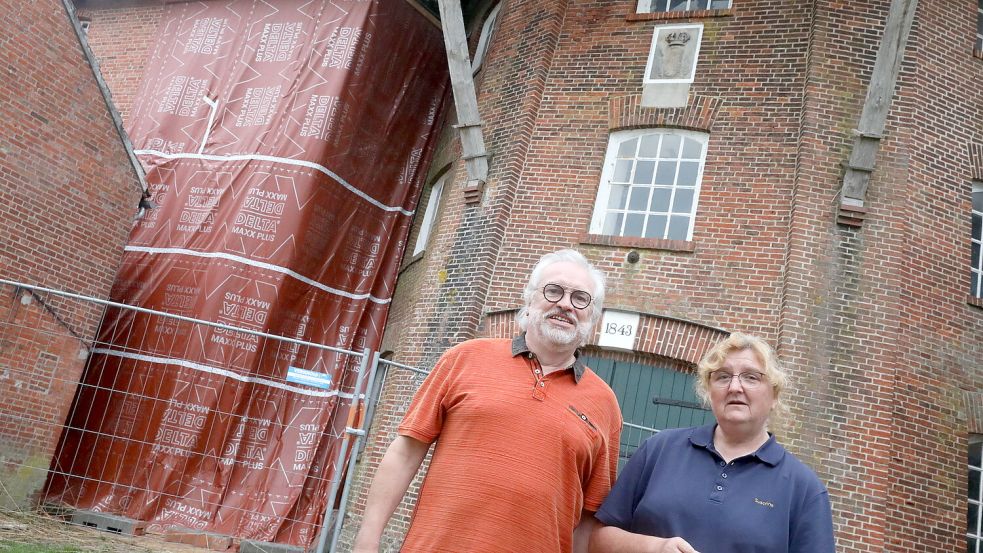 Detlef und Susanne Rongelraths vor der Plane, die das Loch in der Pewsumer Mühle verdeckt. In den vergangenen Wochen waren Handwerker damit beschäftigt, das Mauerwerk abzutragen. Foto: Hock