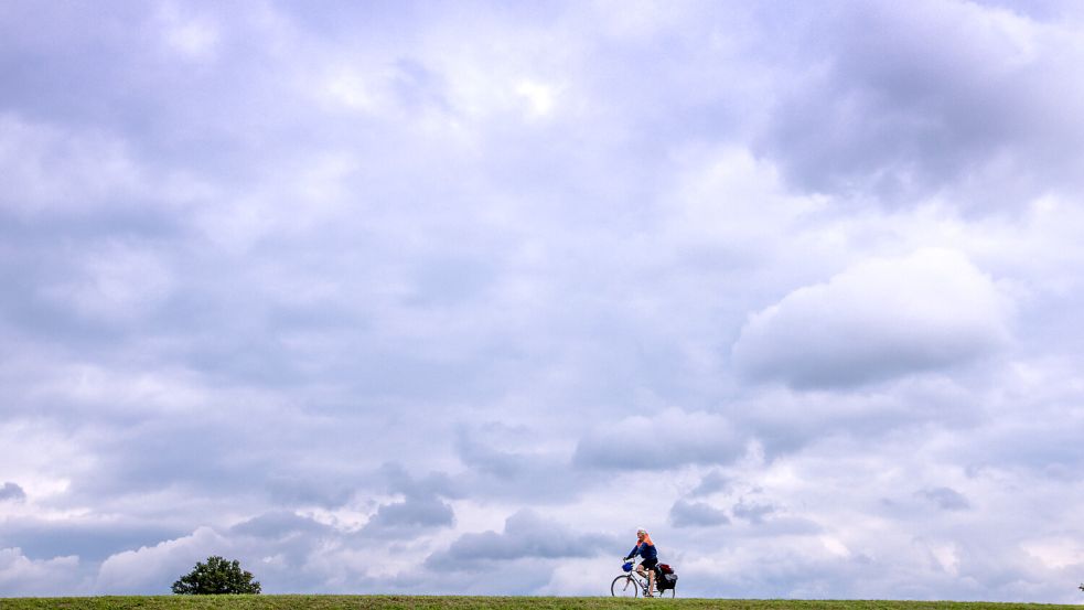 Unter einer dunklen Wolkenkulisse ist ein Radfahrer auf dem Deich unterwegs. Mit sinkenden Temperaturen und dichter Bewölkung kündigt sich in Ostfriesland zum Herbststart ein Wetterwechsel an. Symbolfoto: Büttner/dpa