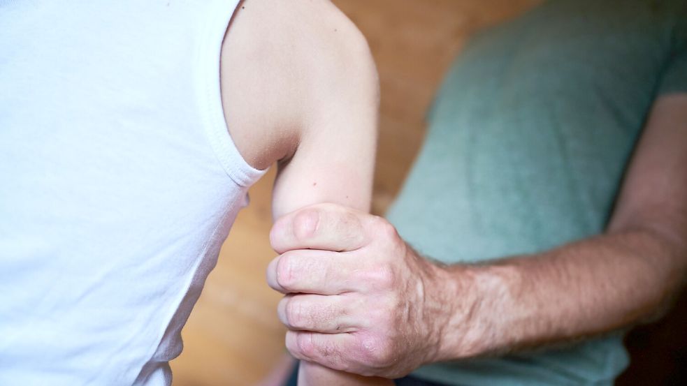 Ein Mann hält ein Kind fest am Arm. Die Zahl der Kindeswohlgefährdungen steigt auch in Ostfriesland. Foto: Riedl/DPA