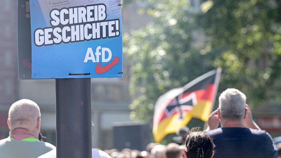 Ein Wahlplakat der AfD hängt an einer Laterne, im Hintergrund ist eine Deutschlandfahne mit Eisernem Kreuz zu sehen. Das Bild entstand im Sommer 2024 in Thüringen. Foto: Albert/dpa